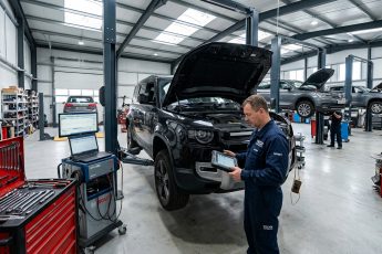 Автосервис Land Rover: внедорожник на подъемнике, механик с планшетом у открытого капота. Современный цех с оборудованием.